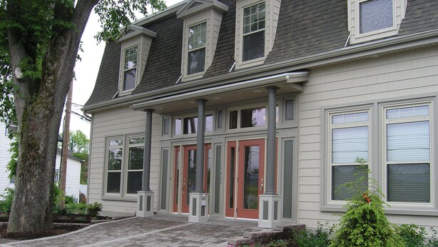 A two-story house with a front porch, a red door, and a brick pathway leading to the entrance. - Windmill walk (Dartmouth)