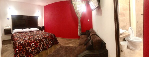 A hotel room with a large bed, a red accent wall, a shower area, and a white toilet.