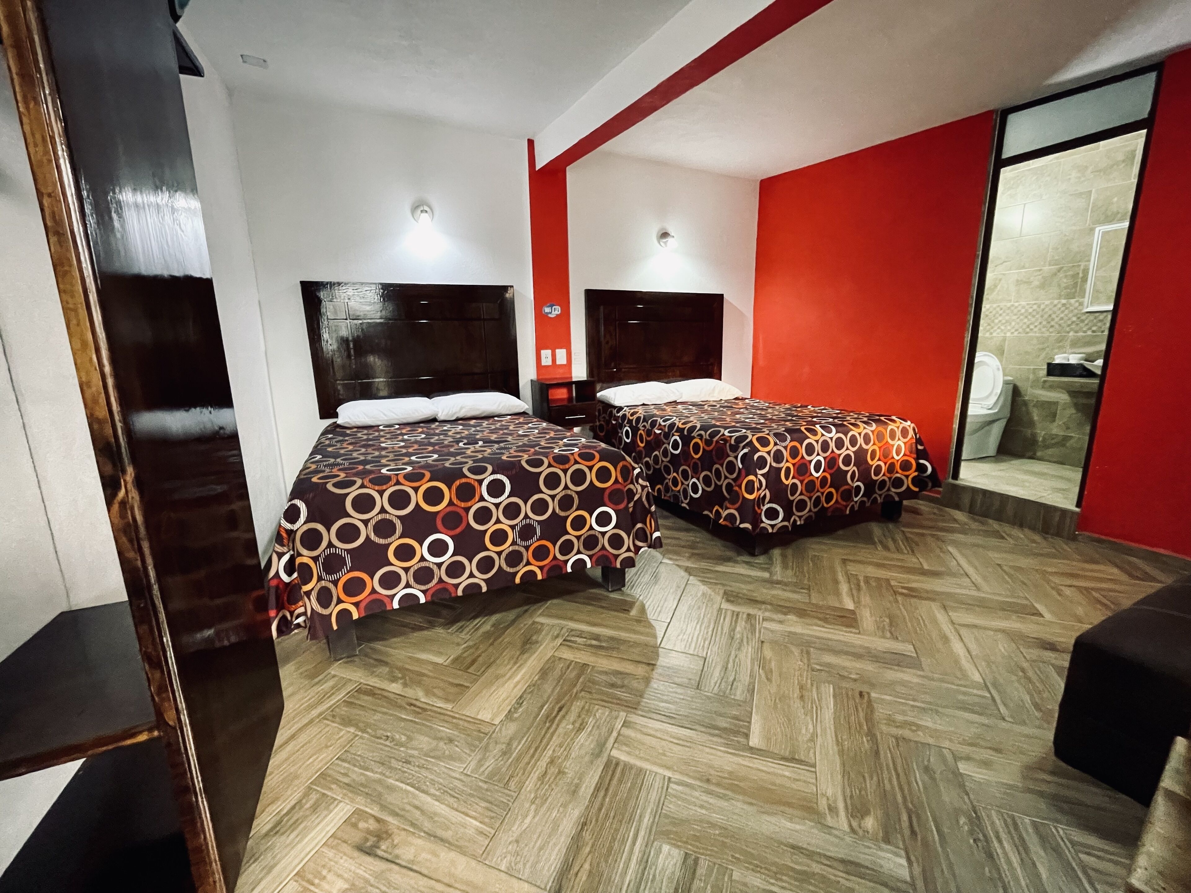 A hotel room with two beds, a wooden floor, and a red accent wall.