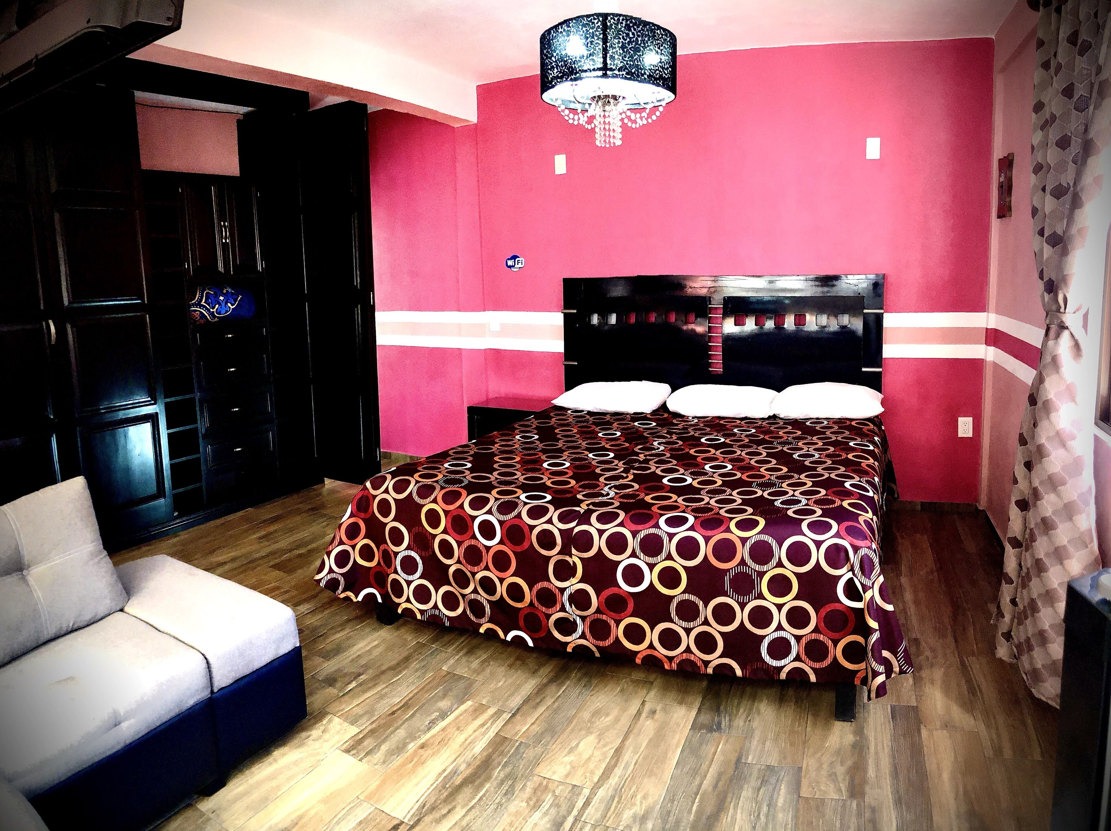 A bedroom with a patterned bedspread, a chandelier, a sofa, and a wardrobe.