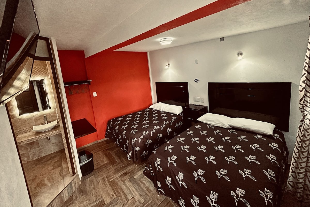 A hotel room with two beds, a small desk, and a mirror.
