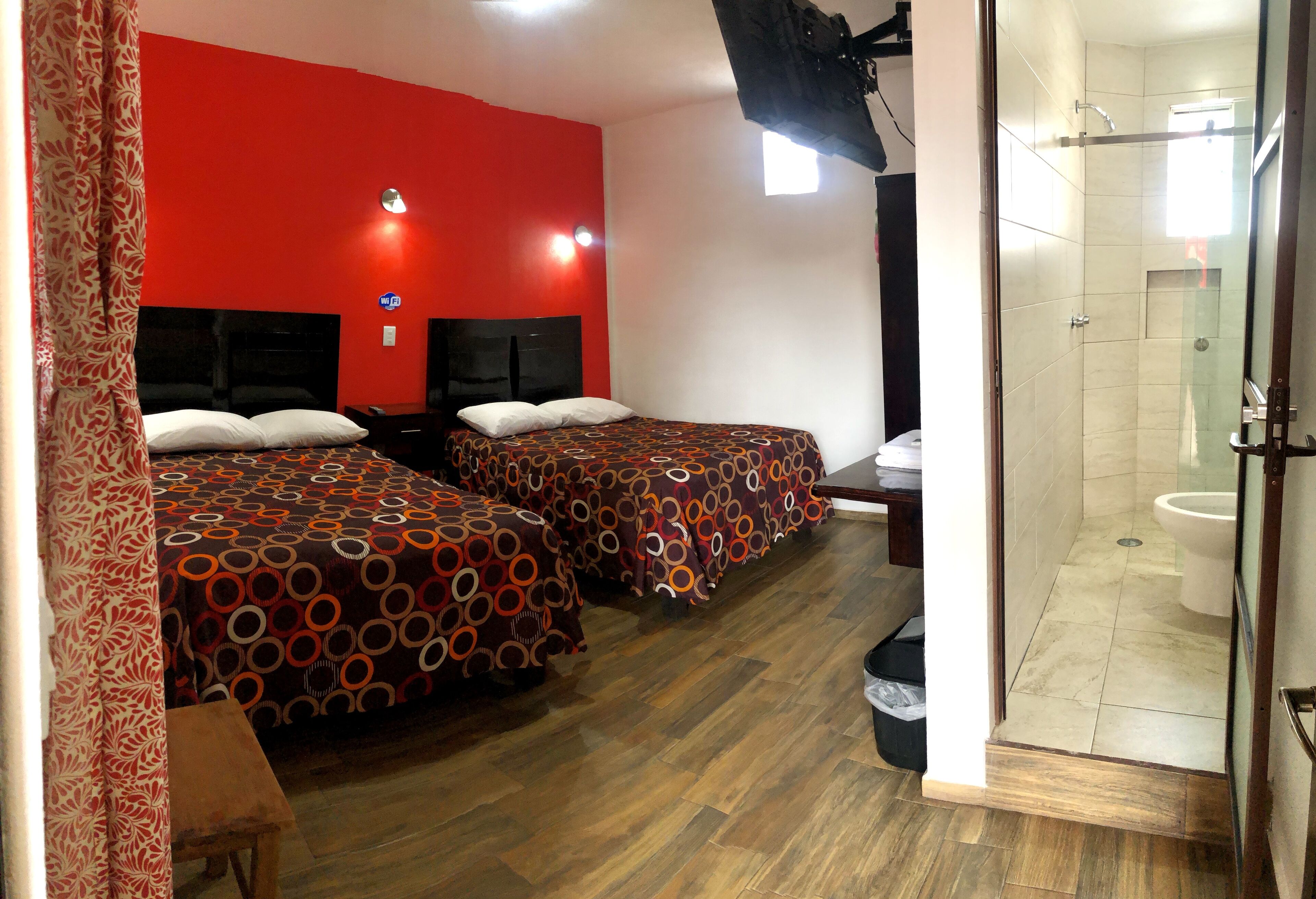A hotel room with two beds, a shower, and a red wall.