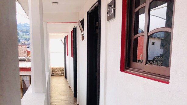 Un pasillo estrecho con suelo de madera, paredes blancas y detalles en rojo. Las puertas están numeradas.