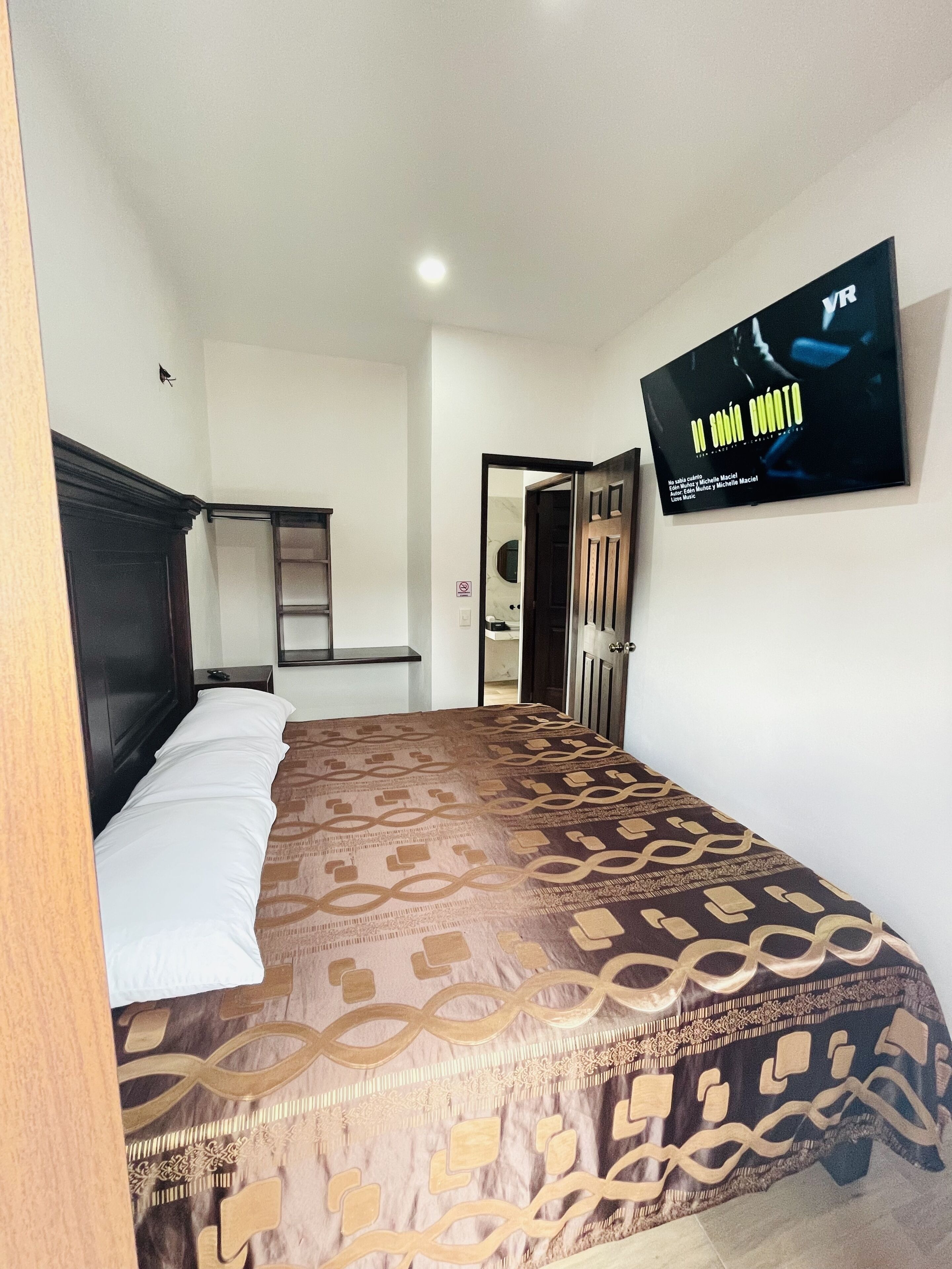 A hotel room with a bed, a TV mounted on the wall, and a door leading to another room.