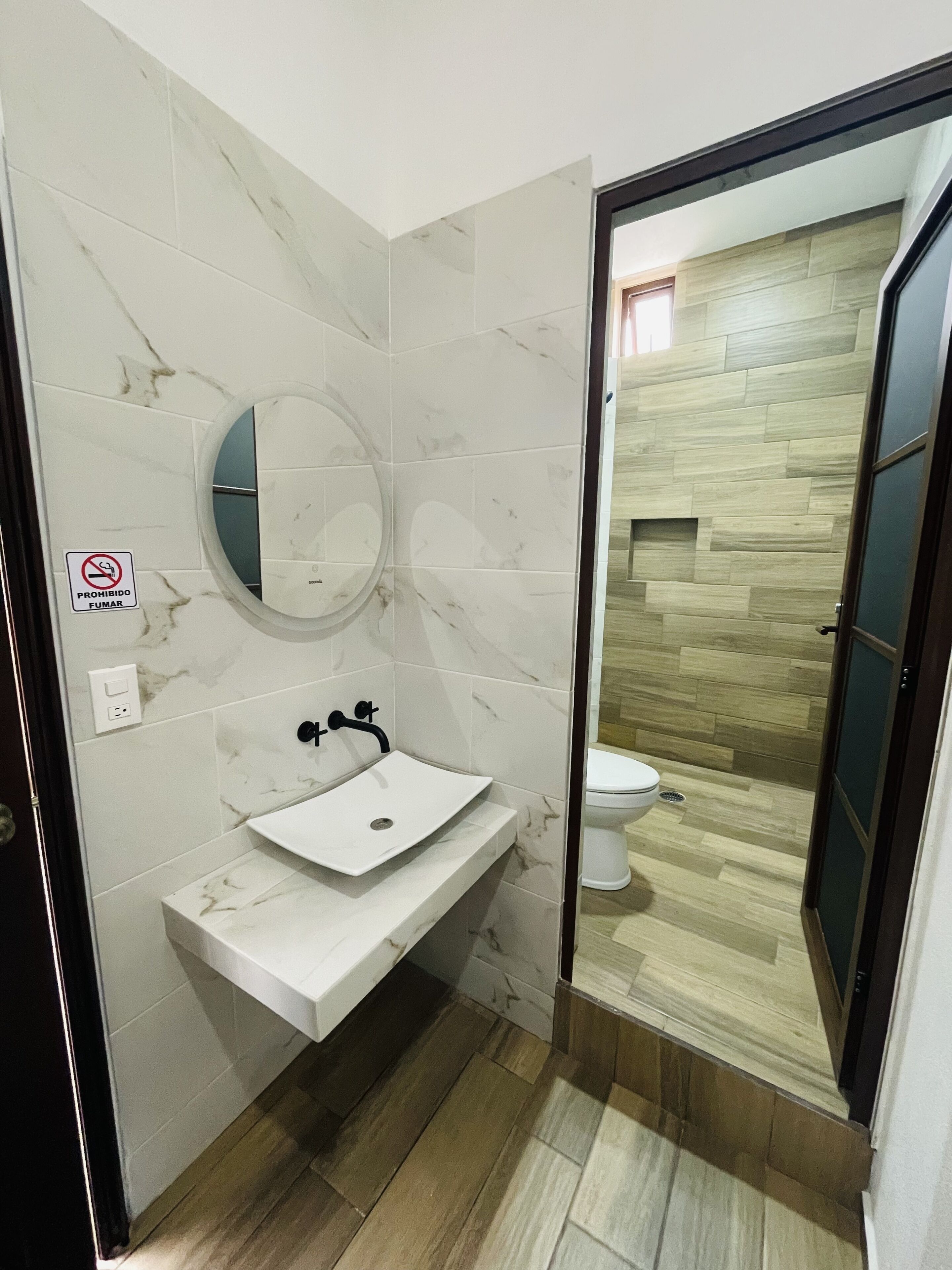A bathroom with a white marble sink, a round mirror, and a toilet.