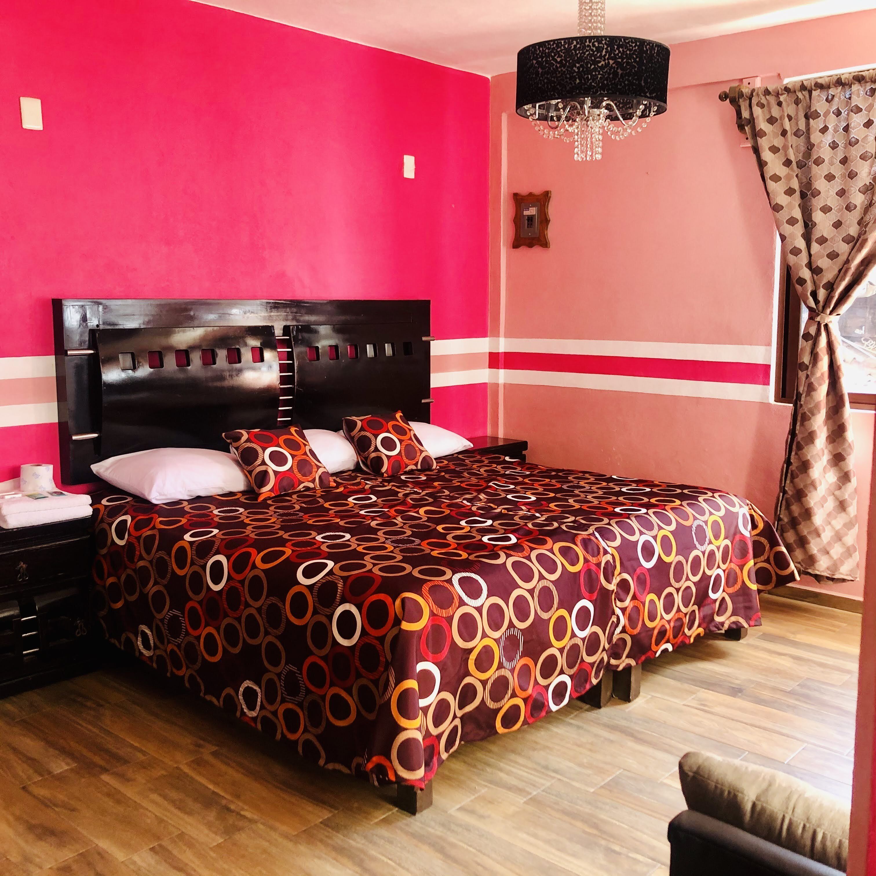 A bedroom with a large bed, a wooden headboard, a chandelier, and a window with curtains.