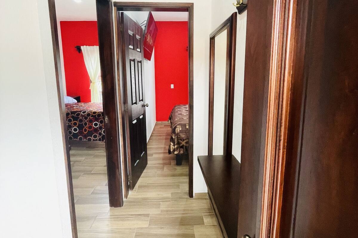 A hallway with a wooden door on the right and a red wall in the background.