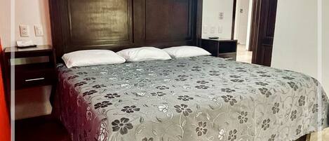 Un dormitorio con cabecera de madera, colcha estampada y suelo de madera.