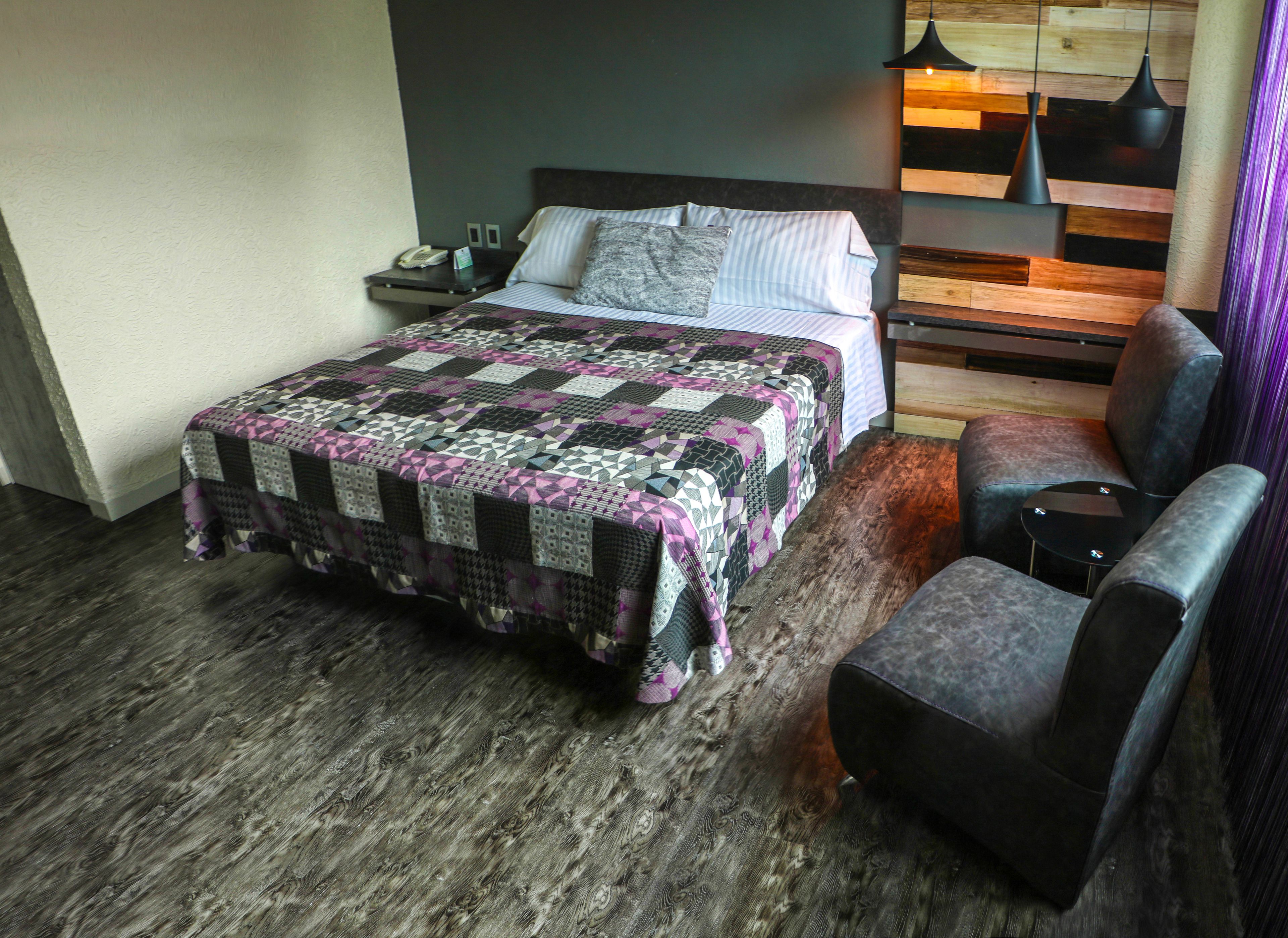 A modern hotel room with a large bed, a small desk, a chair, and a wooden bench.