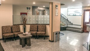 A lobby with patterned seating, a reception desk, a staircase, and a view of the outside. - Hotel La Luna (Mexico City)