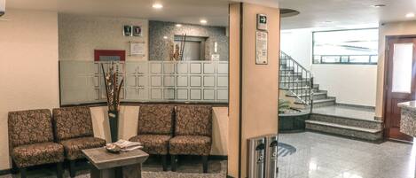 A lobby with patterned seating, a reception desk, a staircase, and a view of the outside.