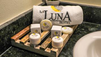Una encimera de baño con un perchero que sostiene una toalla con la etiqueta "La Luna Hotel" y una bandeja con tres frascos de productos de la marca "La Luna".