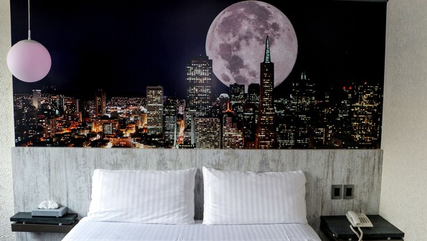 A hotel room with a bed, a nightstand, a phone, and a wall-mounted lamp. - Hotel La Luna (Mexico City)
