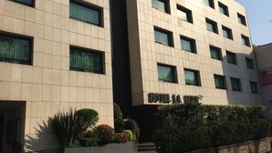A modern hotel building with a sign reading "HOTEL LA JARDIN". It features a clean, geometric facade with multiple windows and a well-maintained garden area in front. - Hotel La Luna (Mexico City)