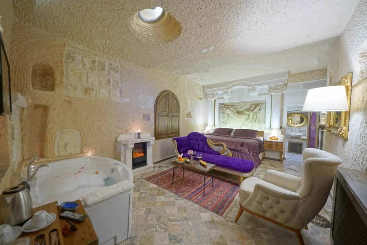 A luxurious room with a large bathtub, a purple sofa, and a fireplace.