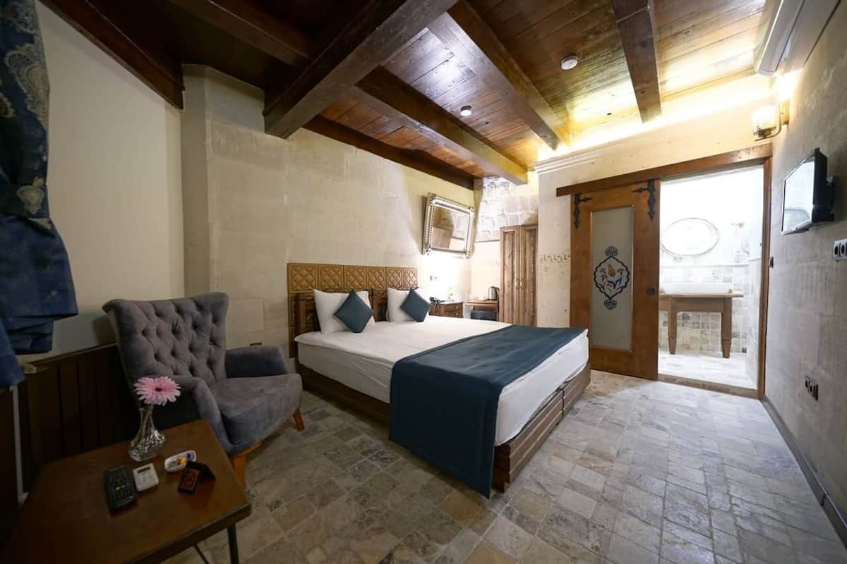 A bedroom with a bed, a chair, a table with a vase, and a door leading to an outdoor area.
