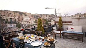 A rooftop dining area with a table set for breakfast, overlooking a mountainous landscape. - Arte Cave Hotel (Ürgüp)