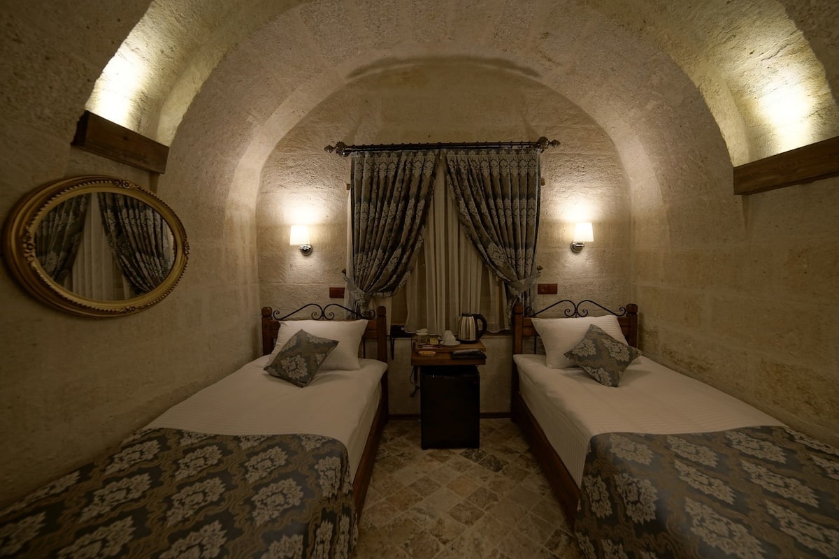 A room with two beds, a round mirror, and a small table with a kettle.