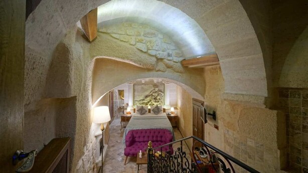 A bedroom with a stone archway, a bed, a purple sofa, and a staircase. - Arte Cave Hotel (Ürgüp)