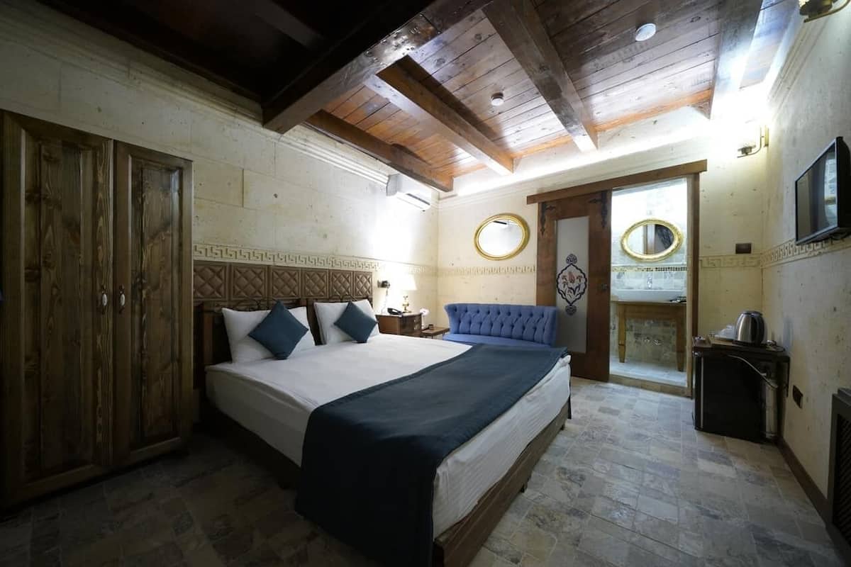 A bedroom with a large bed, wooden wardrobe, and a small kitchenette.
