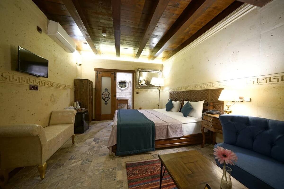 A room with a bed, a sofa, a TV, a mirror, and a small table with a vase.