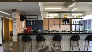 Un espace bar moderne avec un comptoir, des tabourets de bar et un coin salon doté de coussins verts.