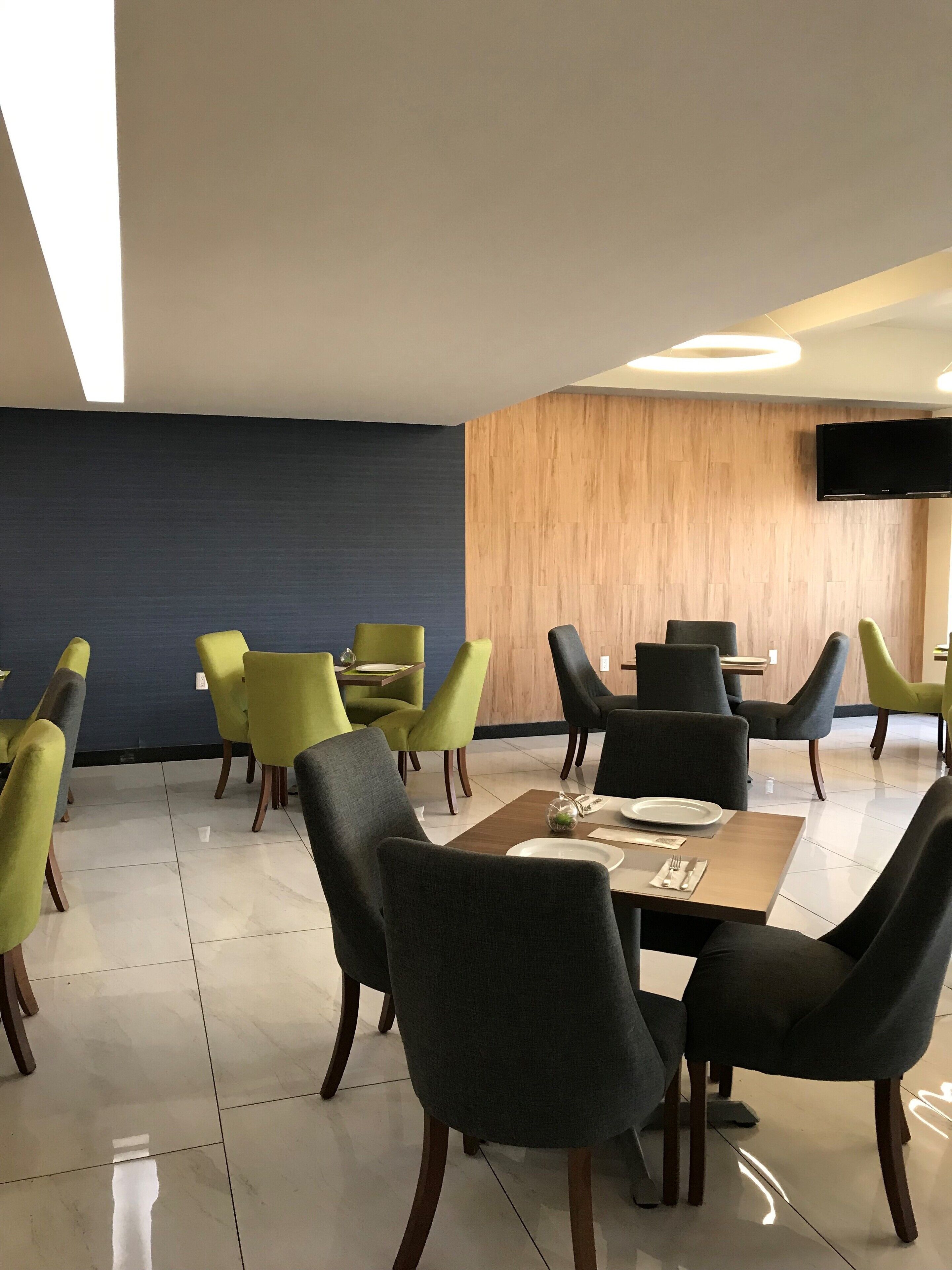 A modern dining area with a mix of green and black chairs, a wooden table, and a flat-screen TV mounted on the wall.