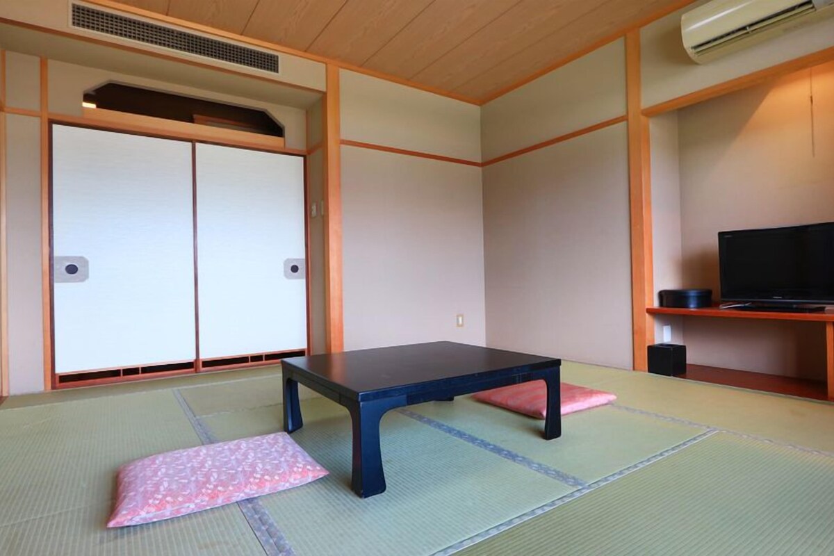 Een traditionele Japanse kamer met tatami vloerbedekking, een lage tafel, een televisie en een kast.