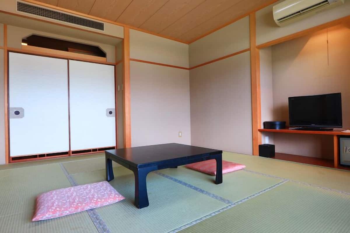 A traditional Japanese room with tatami flooring, a low table, a television, and a cabinet.