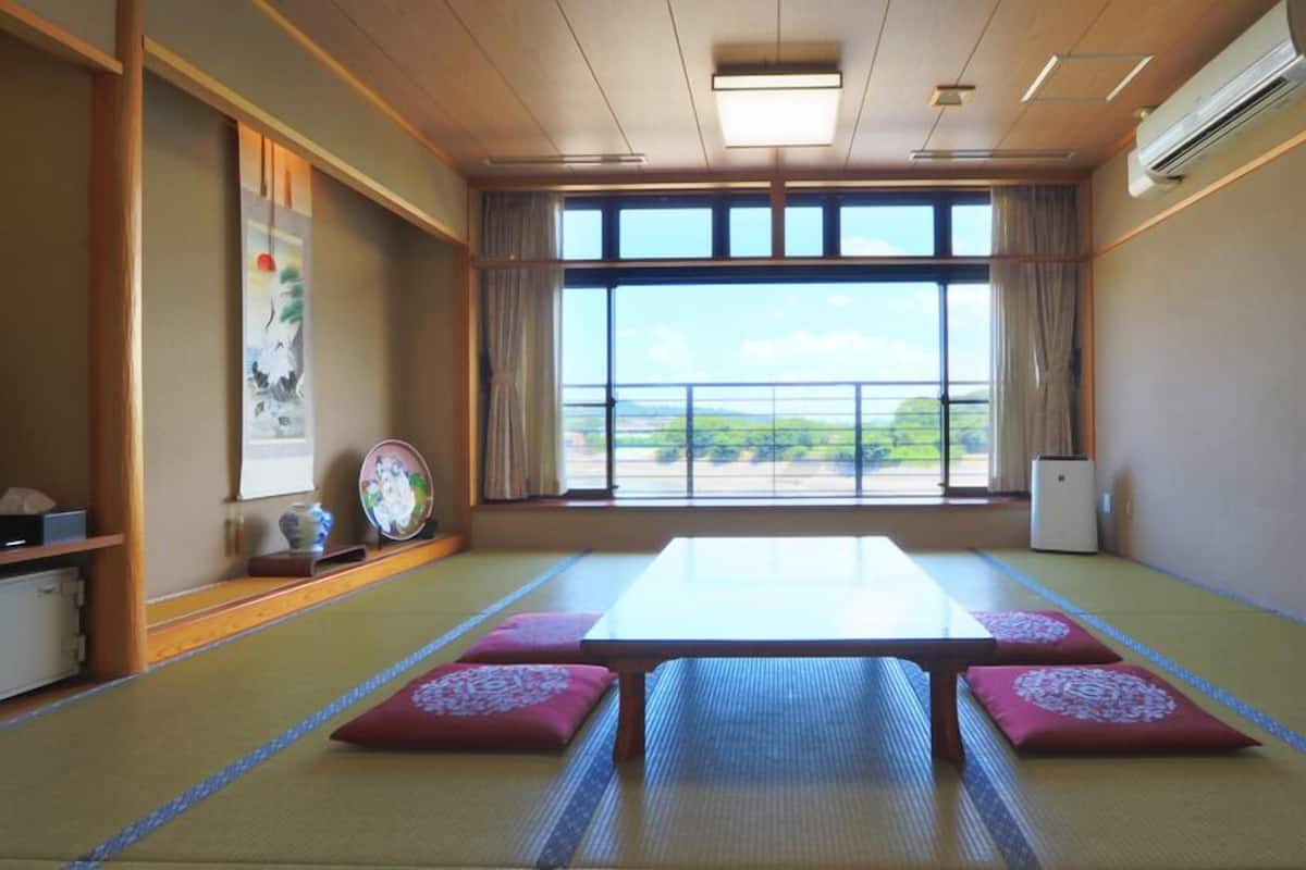 A tatami mat room with a view of a green landscape, a table, and a traditional Japanese painting.