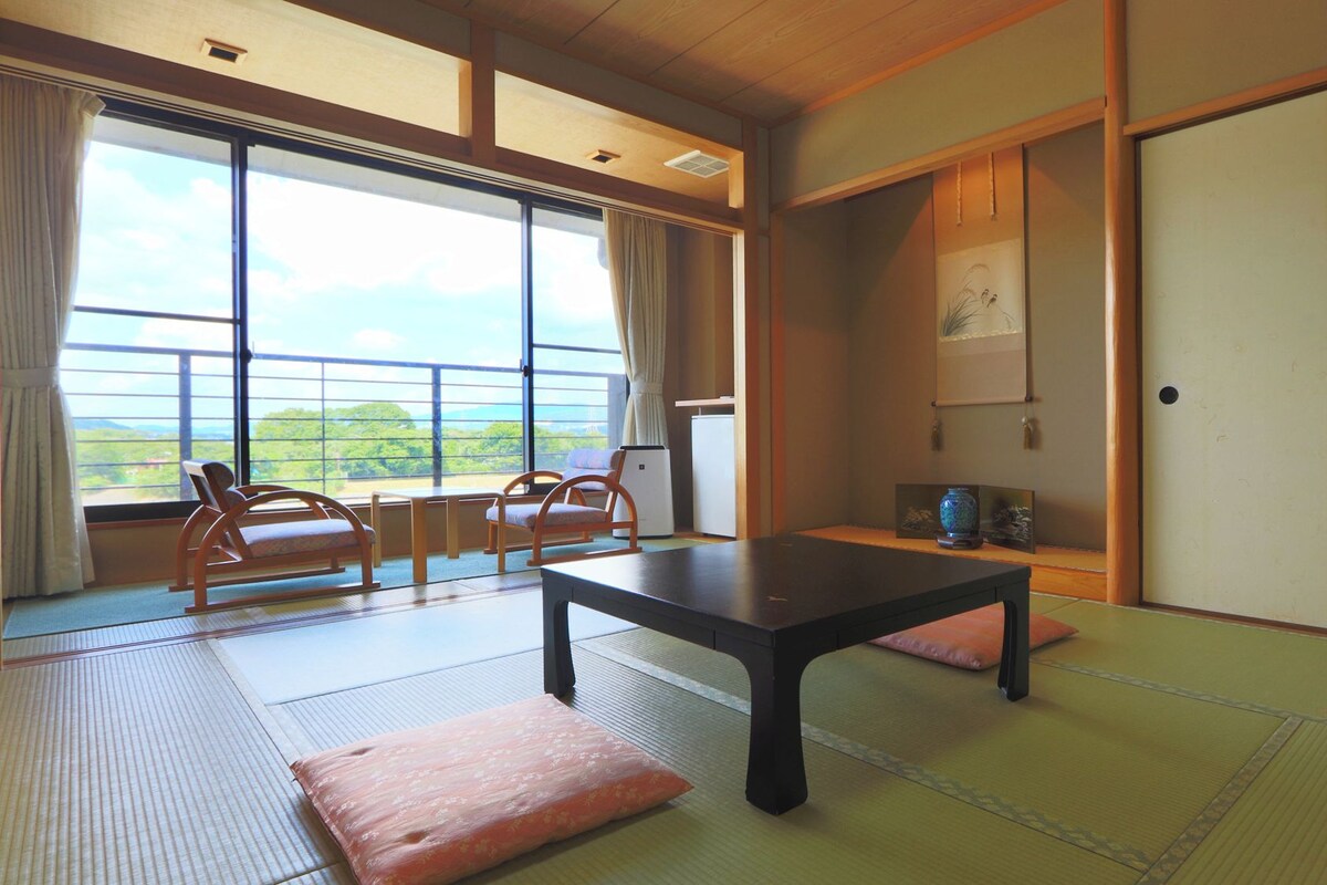 Een traditionele Japanse kamer met tatami vloerbedekking, een lage tafel en uitzicht op het omliggende landschap.