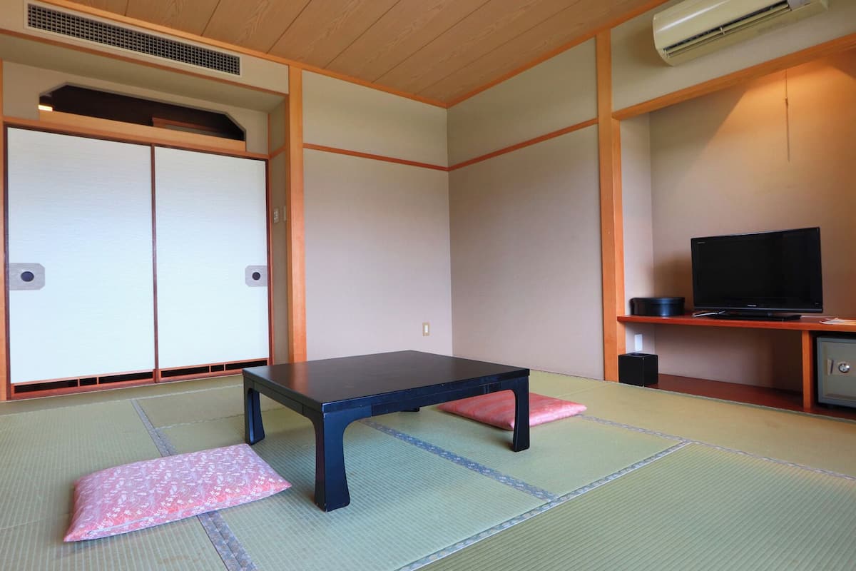 A traditional Japanese room with tatami flooring, a low table, a television, and a cabinet.