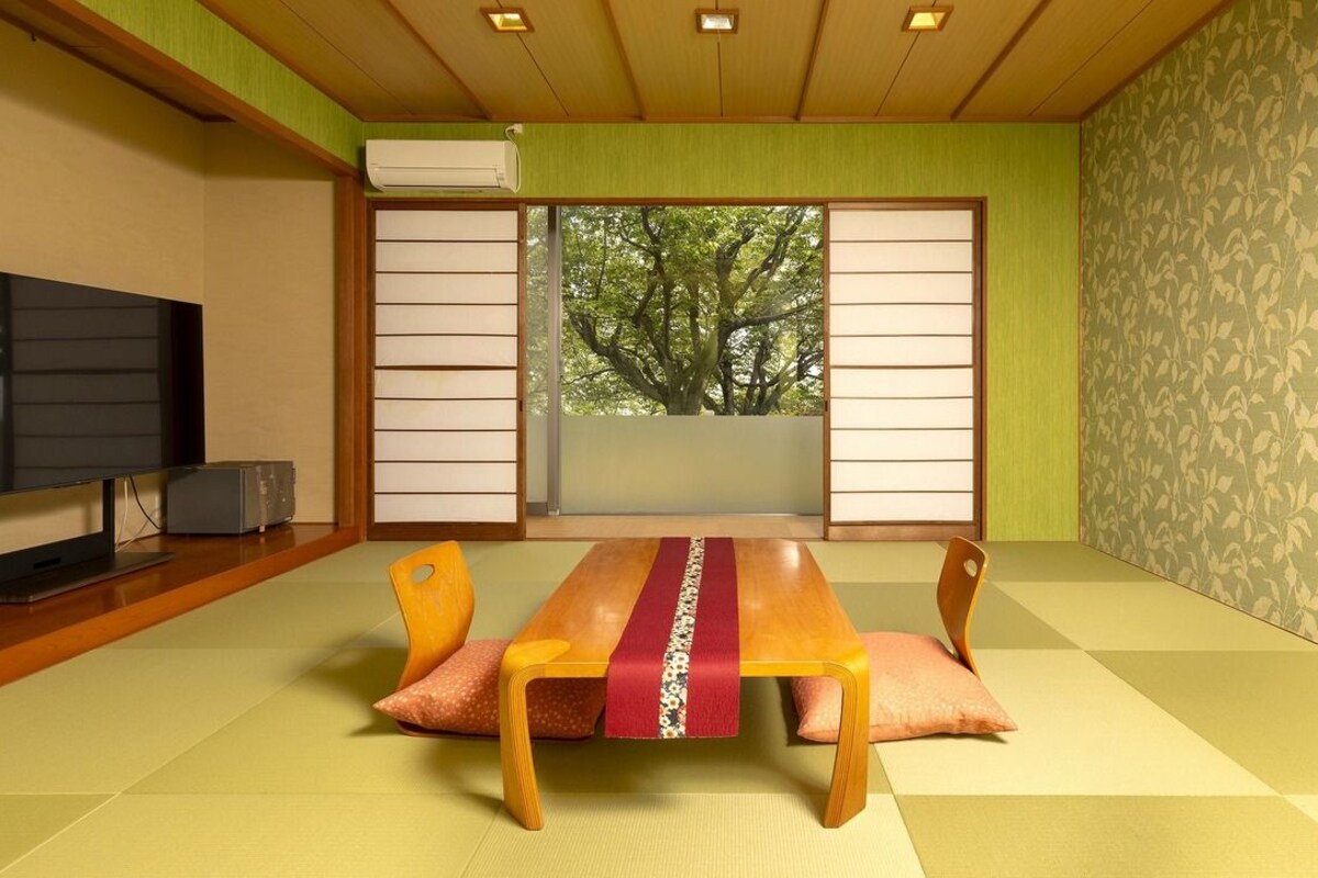 A traditional Japanese-style room with tatami flooring, a low table with cushions, a television, and sliding shoji doors.