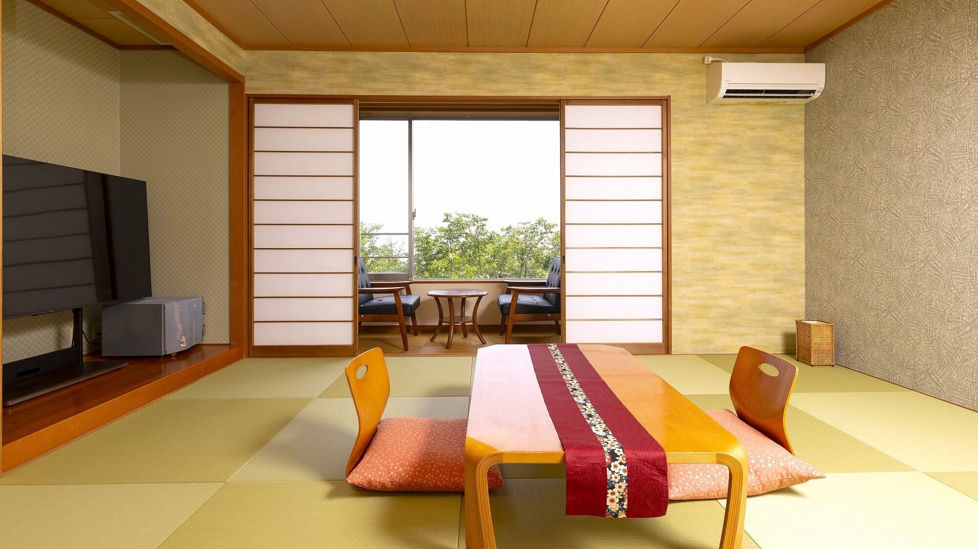 A tatami mat room with a low table, chairs, a television, and sliding doors leading to a balcony.