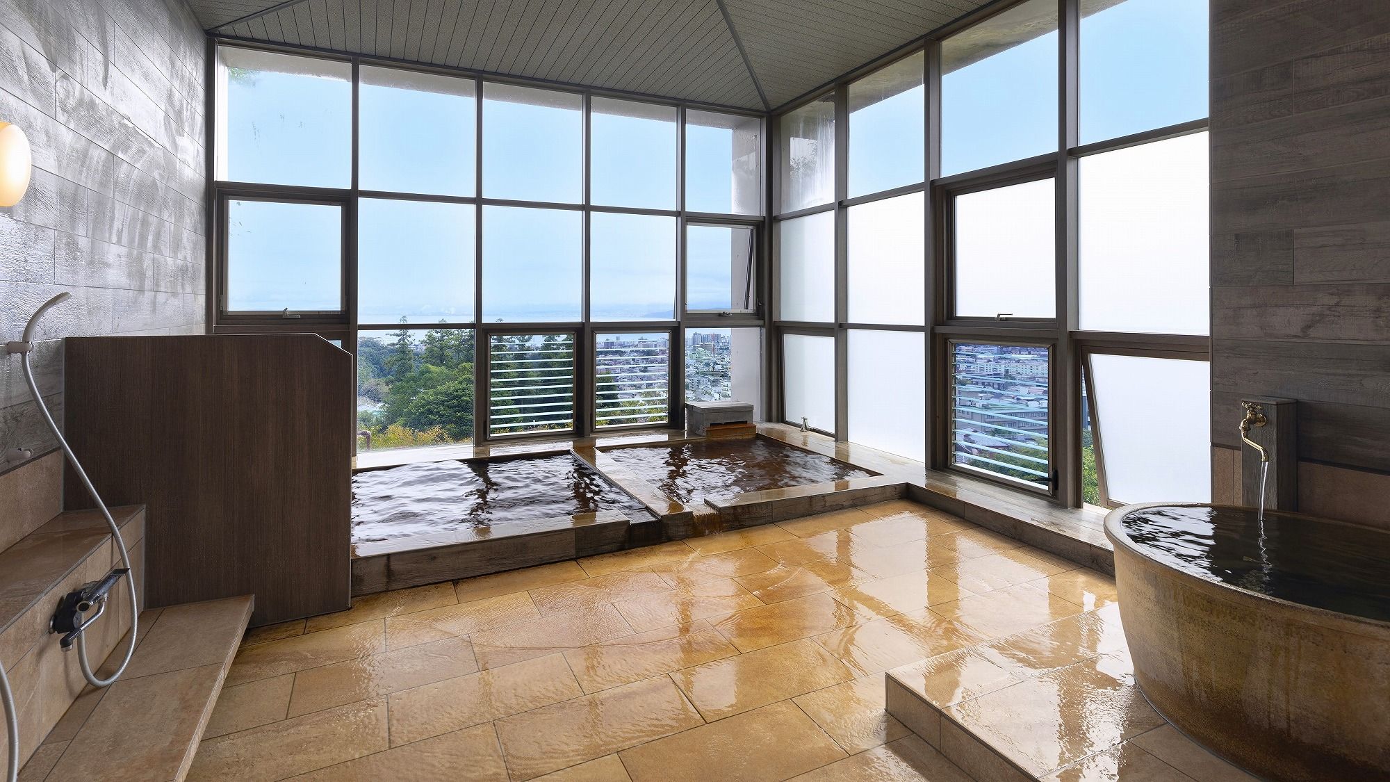 A spacious room with large windows, a hot tub, and a shower area.