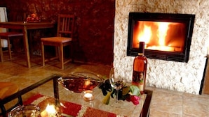 A cozy room with a stone fireplace, a dining table with chairs, and a candle-lit table setting. - Paliokastro Guesthouse (Xylokastro-Evrostina)