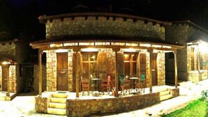A stone building with a covered patio area featuring outdoor seating. - Paliokastro Guesthouse (Xylokastro-Evrostina)