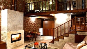 A cozy interior with a stone fireplace, wooden staircase, and a dining area. - Paliokastro Guesthouse (Xylokastro-Evrostina)