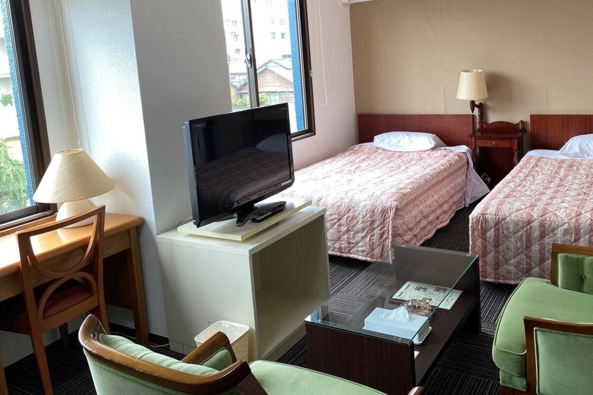 Una camera d'albergo con due letti, una televisione, una scrivania con una lampada e una poltrona verde.