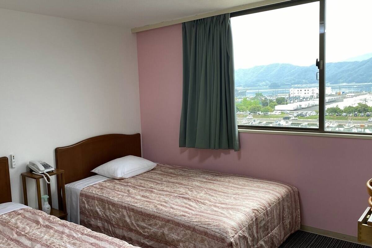 Camera d'albergo con due letti, un telefono e una finestra vista città e montagne.