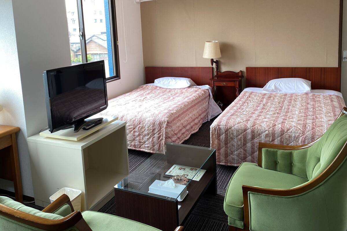 Una camera d'albergo con due letti, una televisione, una scrivania con lampada e una sedia.