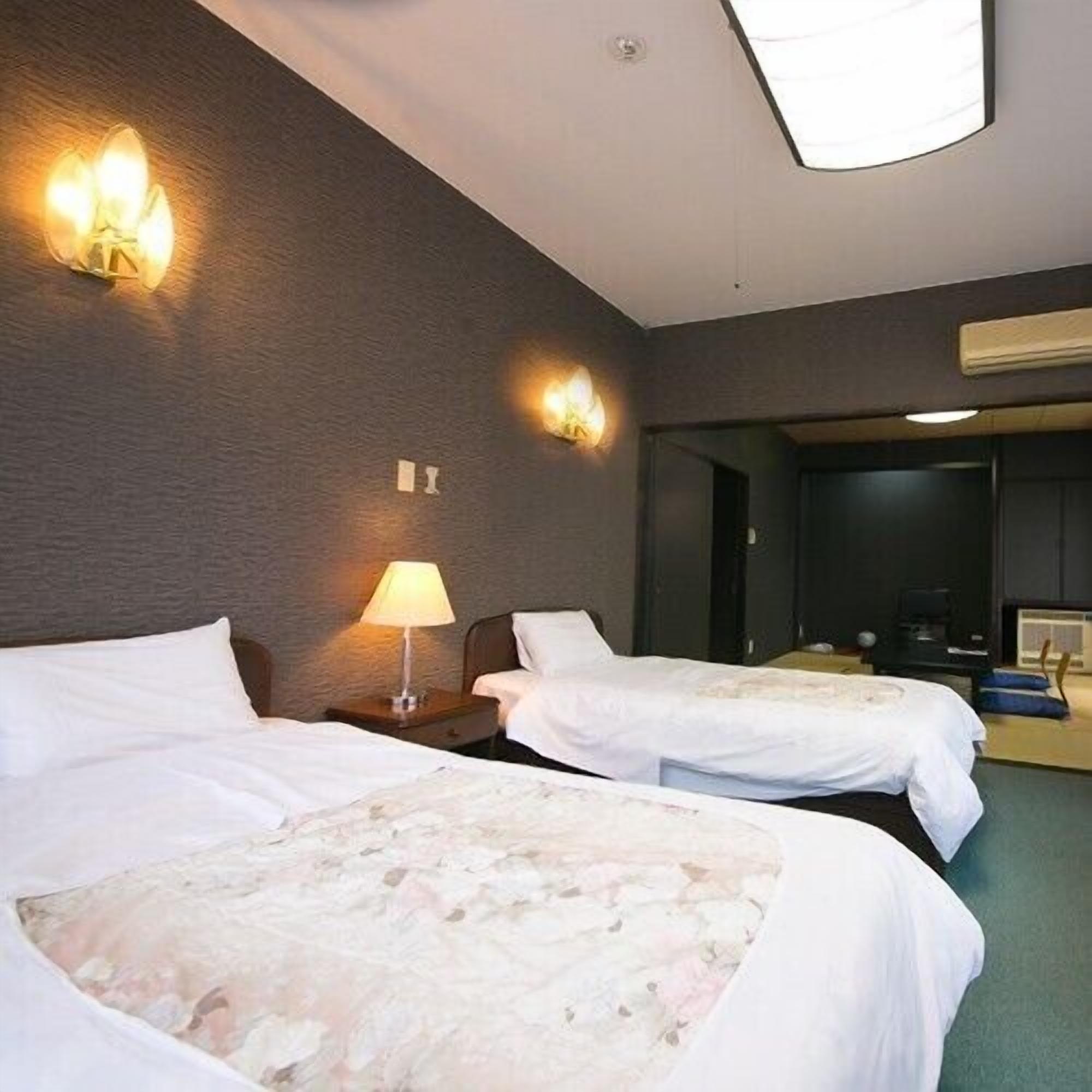 A hotel room with two beds, a nightstand with a lamp, and a wall-mounted light fixture.