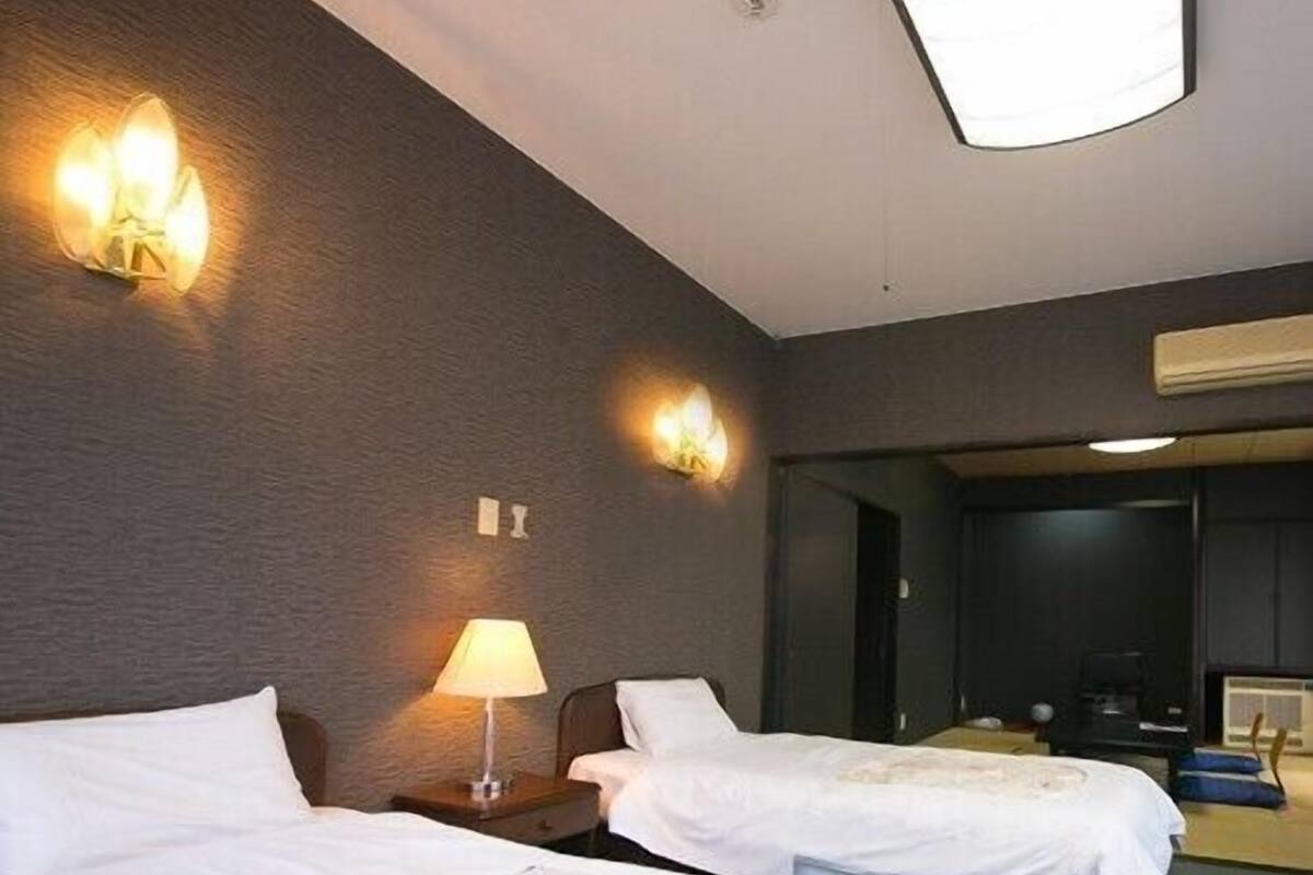 A hotel room with two beds, a nightstand with a lamp, and a wall-mounted light fixture.