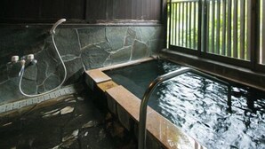 A stone-walled hot tub with a wooden deck, a metal ladder, and a window with a view of greenery. - Hosenji Onsen Ryusenkaku (Kokonoe)