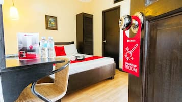 A hotel room with a bed, a desk, and a chair. There is a door with a red sign that says "Make Up Room".