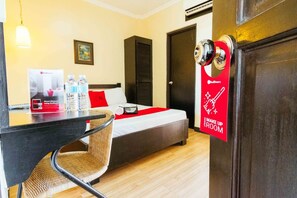 A hotel room with a bed, a desk, and a chair. There is a door with a red sign that says "Make Up Room".