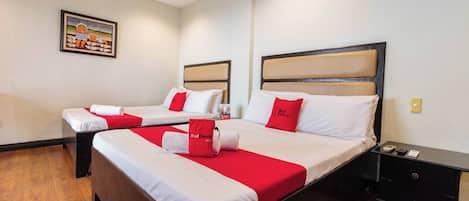 A hotel room with two beds, each with a red pillow and a white bedspread. There is a painting on the wall and a small table with a phone and a remote control.