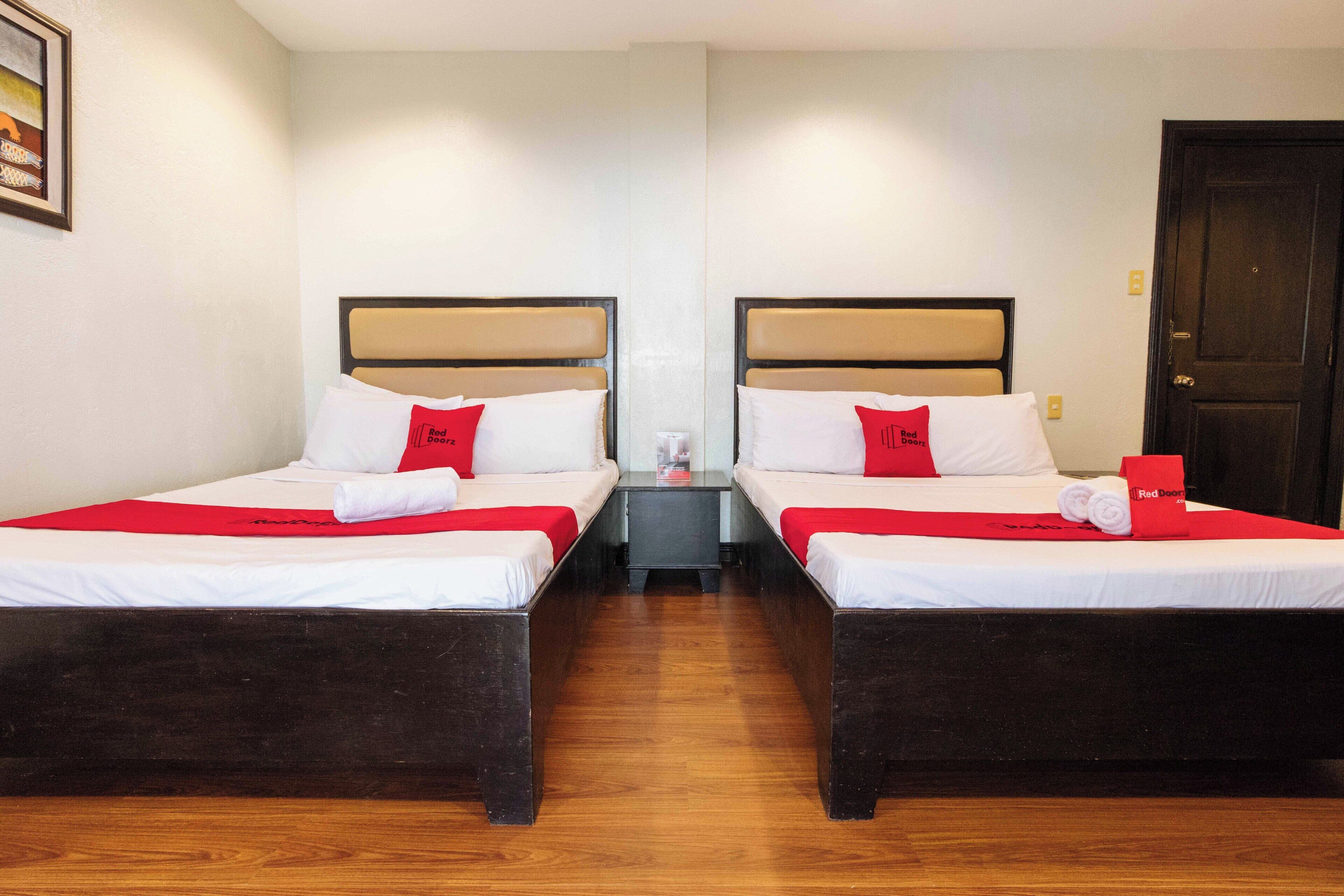 Habitació d'hotel amb dos llits, una tauleta de nit, una porta i un quadre a la paret.