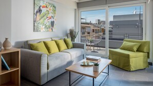 A modern living room with a grey sofa, a green armchair, a wooden coffee table, and a large window offering a city view. - 12 Keys Athens Apartments (Athens)