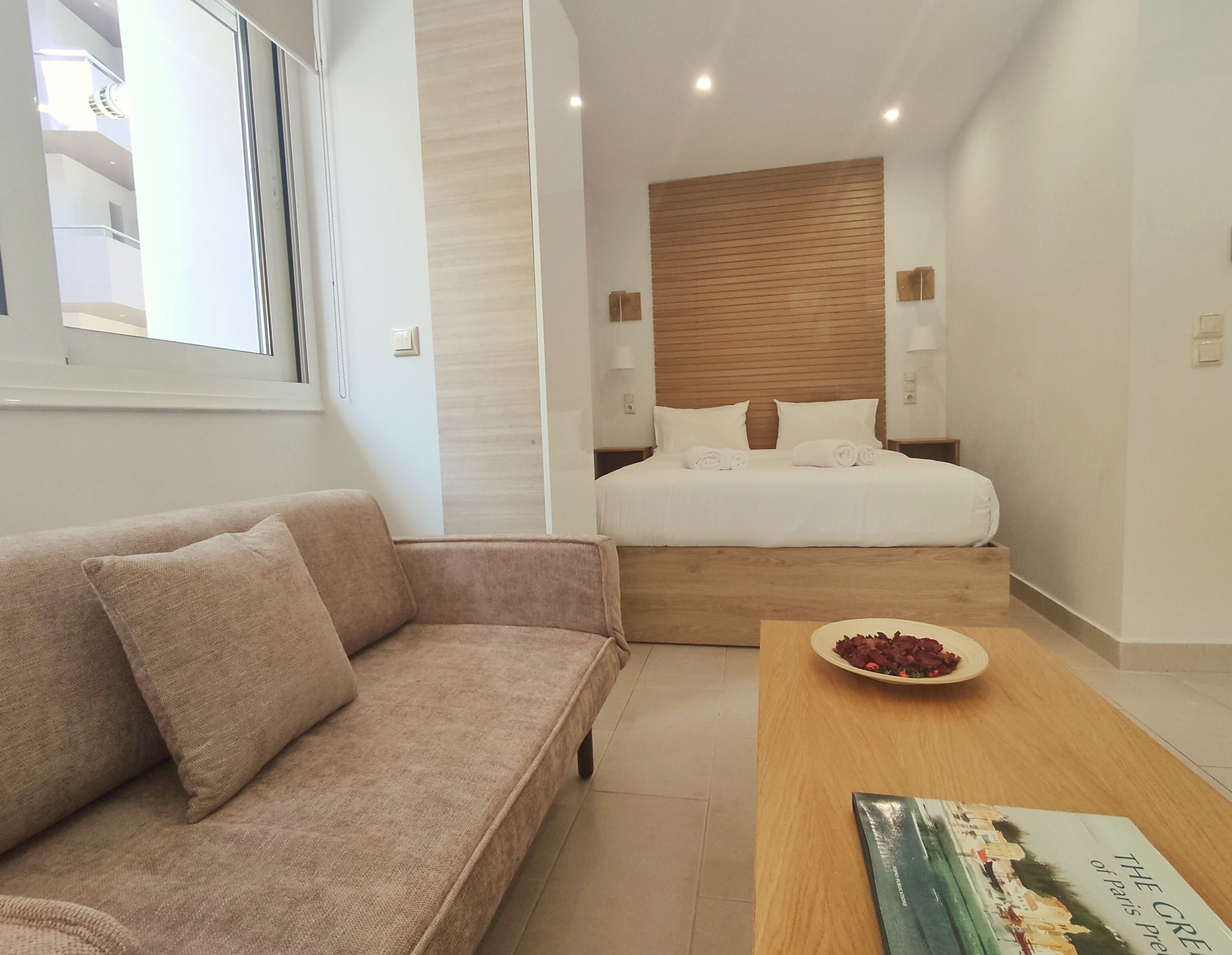 A modern hotel room with a bed, a sofa, and a wooden coffee table.